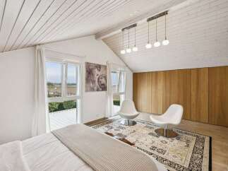 This stunning bedroom boasts a bright and airy atmosphere with its high, white-paneled ceilings and large windows that flood the space with natural light.