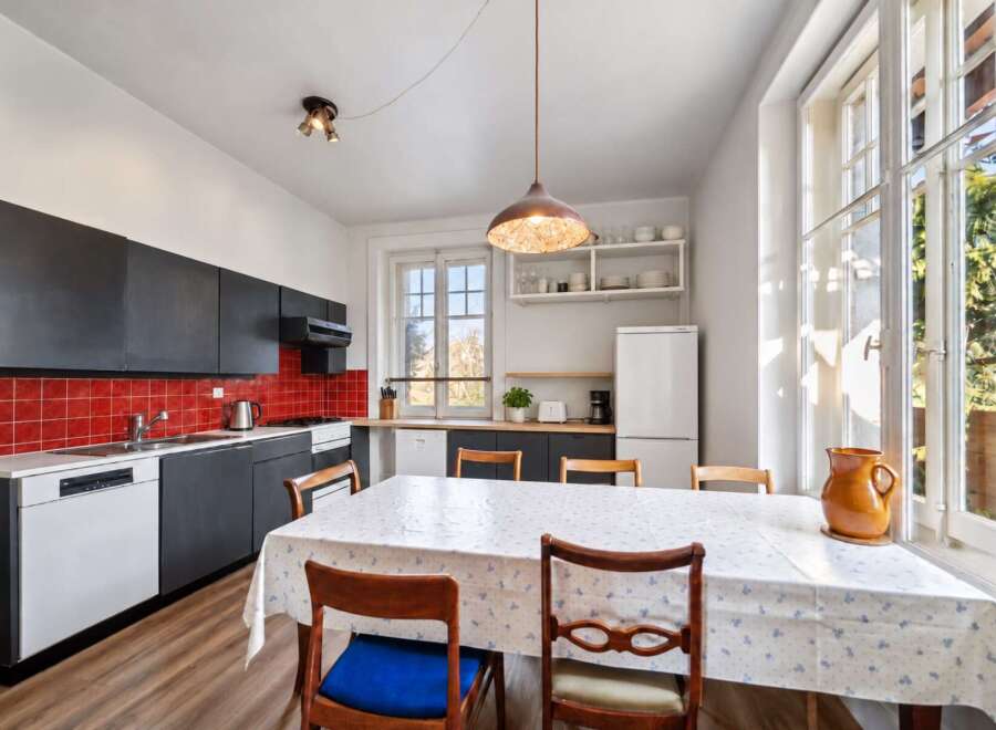 This charming kitchen features sleek black cabinetry contrasted with a vibrant red tiled backsplash, offering a modern and stylish aesthetic.