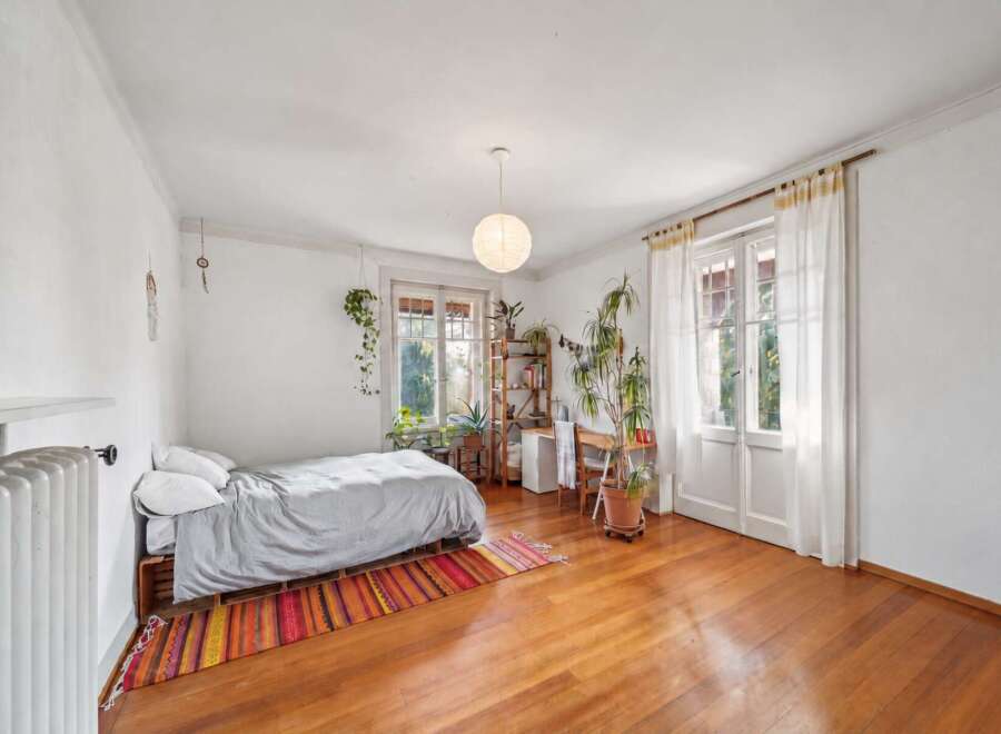 Bright and airy bedroom featuring a cozy bed with a grey duvet, set on a wooden pallet base and adorned with a colorful striped rug.
