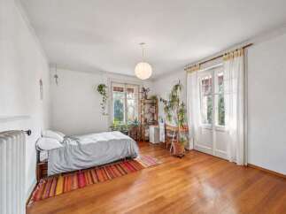 Bright and airy bedroom featuring a cozy bed with a grey duvet, set on a wooden pallet base and adorned with a colorful striped rug.