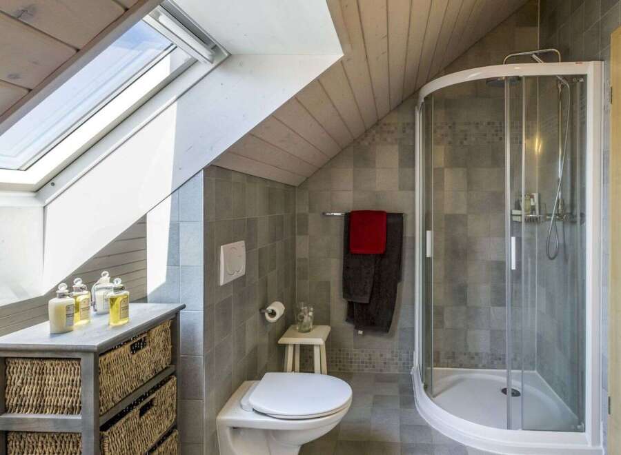 This charming bathroom features a modern design with a unique sloped ceiling and a skylight that floods the space with natural light.