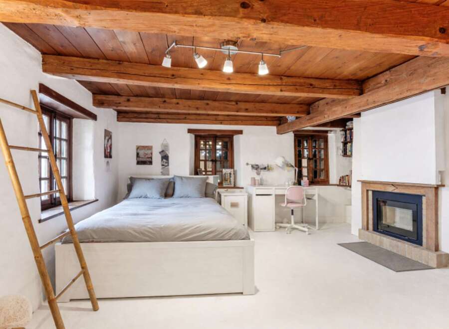 This charming bedroom boasts a rustic aesthetic with exposed wooden beams and a cozy fireplace.