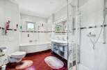 Step into this bright and airy bathroom, featuring pristine white tiles and a stylish red tile floor.