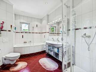 Step into this bright and airy bathroom, featuring pristine white tiles and a stylish red tile floor.