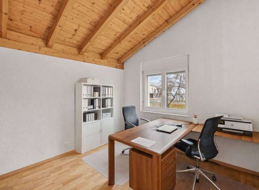 This stunning home office features a beautiful wooden ceiling and a large window that provides ample natural light.