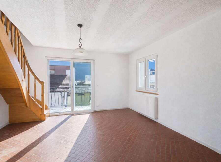 Discover this bright and airy living space, featuring a beautiful wooden staircase and a charming pendant light.