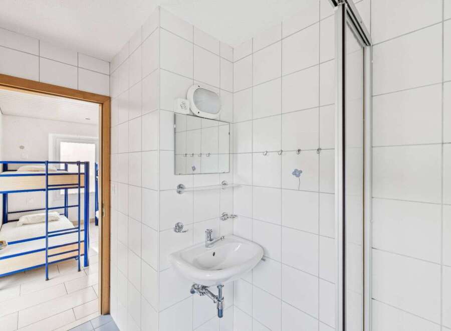This property features a clean and modern bathroom with white tiled walls and a sleek sink.