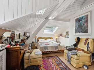 This charming bedroom boasts a unique architectural design with its sloped ceilings and skylight, creating a bright and airy atmosphere.