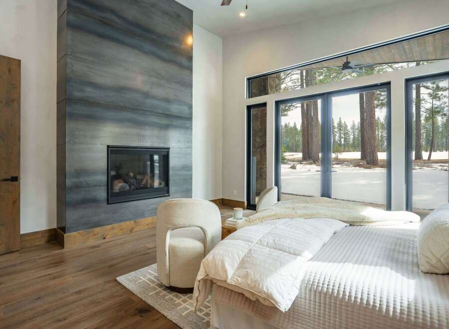 Experience luxury living in this stunning bedroom featuring a modern fireplace and expansive windows.