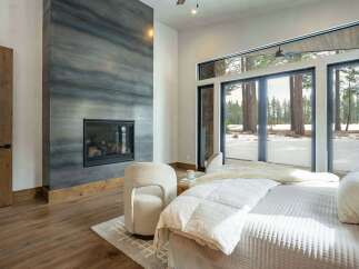 Experience luxury living in this stunning bedroom featuring a modern fireplace and expansive windows.