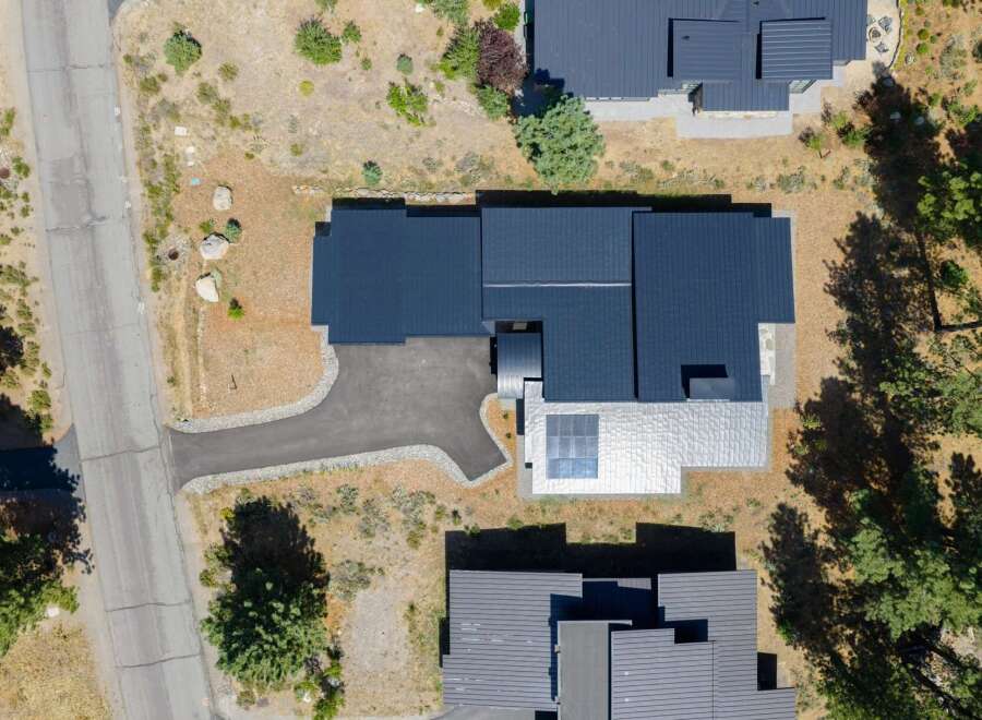 Experience modern luxury with this stunning aerial view of a contemporary home featuring a sleek dark metal roof and a unique silver metal facade.