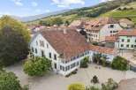 Discover this stunning property featuring a grand white house with a classic terracotta tile roof, nestled amidst charming village architecture and rolling vineyards.