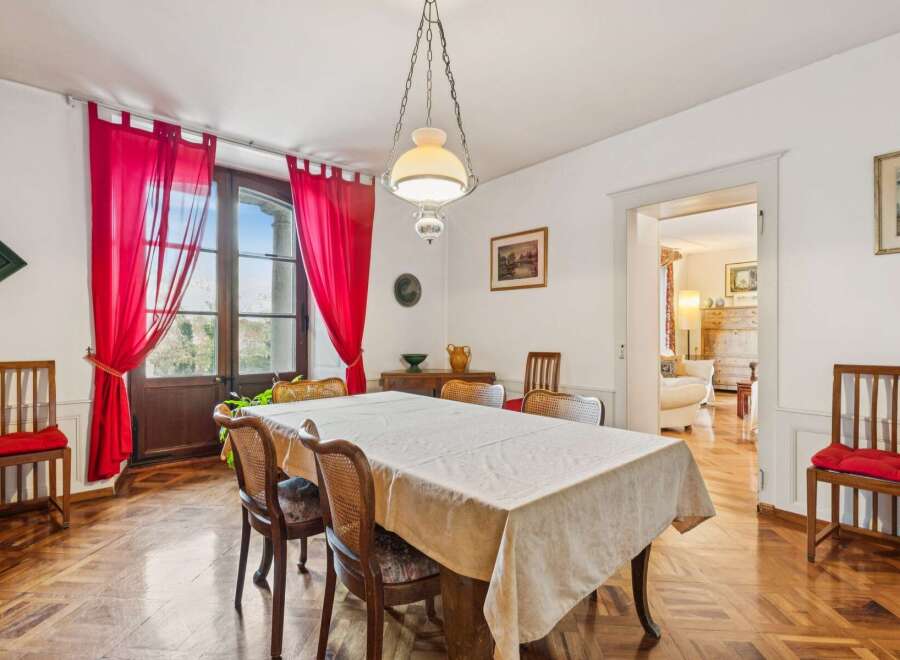This elegant dining room features a large table draped in a light-colored tablecloth, surrounded by classic wooden chairs with cane backs and upholstered seats.