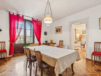 This elegant dining room features a large table draped in a light-colored tablecloth, surrounded by classic wooden chairs with cane backs and upholstered seats.
