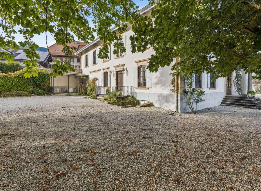 Discover this charming property featuring a spacious gravel driveway leading to a classic white house with traditional shutters and elegant windows.