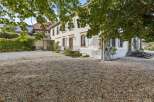 Discover this charming property featuring a spacious gravel driveway leading to a classic white house with traditional shutters and elegant windows.