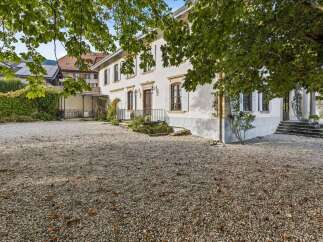 Discover this charming property featuring a spacious gravel driveway leading to a classic white house with traditional shutters and elegant windows.