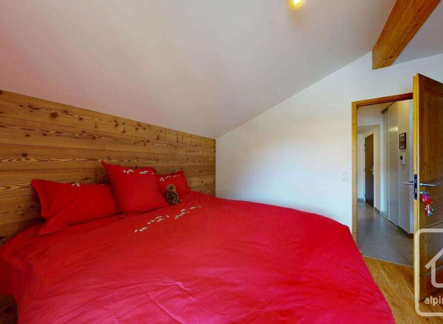 Discover the charm of this cozy bedroom featuring a striking wooden accent wall and a vibrant red bedspread.