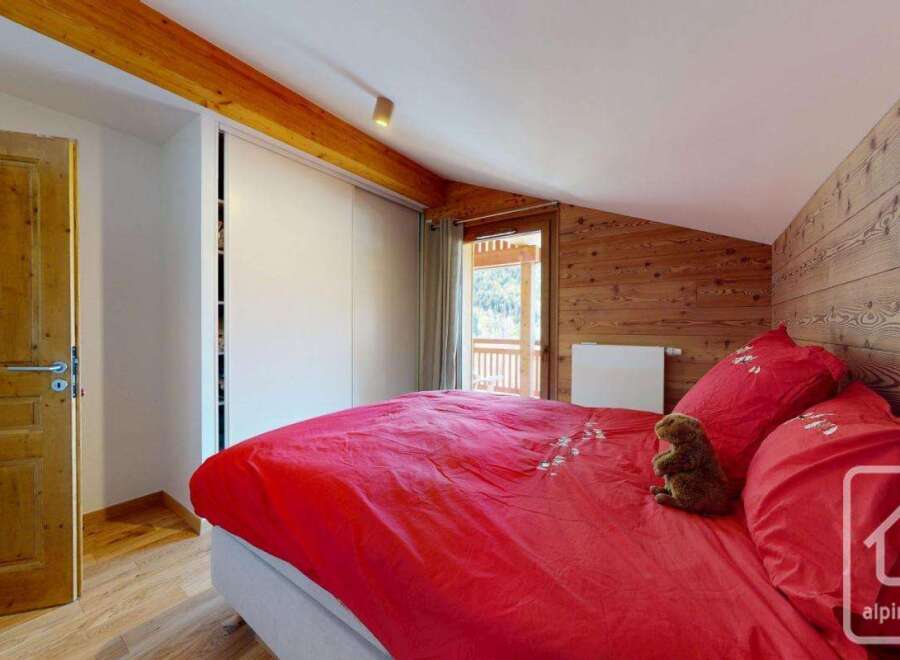 Discover the charm of this cozy bedroom, featuring a vibrant red bedspread and rustic wooden accents.