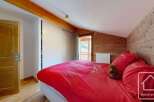 Discover the charm of this cozy bedroom, featuring a vibrant red bedspread and rustic wooden accents.