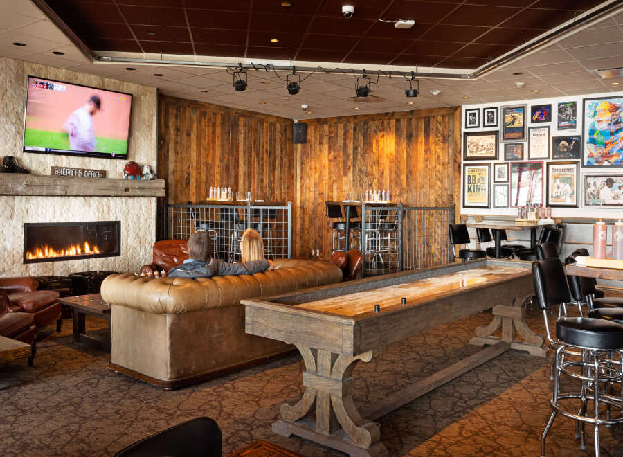 This cozy lounge features a warm fireplace, comfortable seating, and a shuffleboard table, perfect for relaxing and socializing.