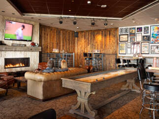 This cozy lounge features a warm fireplace, comfortable seating, and a shuffleboard table, perfect for relaxing and socializing.