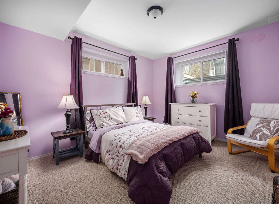This charming bedroom boasts a serene ambiance with its soft purple walls and cozy carpet flooring.