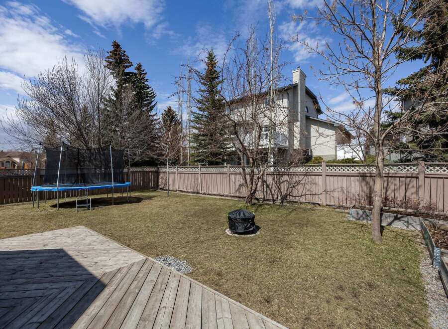 Enjoy outdoor living in this beautiful backyard! This property features a spacious deck, perfect for entertaining, and a lush lawn with a trampoline.