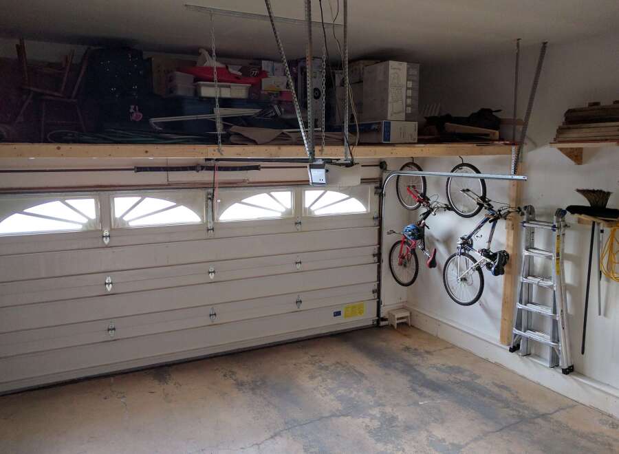 This garage offers ample storage space with overhead shelving and wall-mounted bike racks, perfect for organizing tools and equipment.
