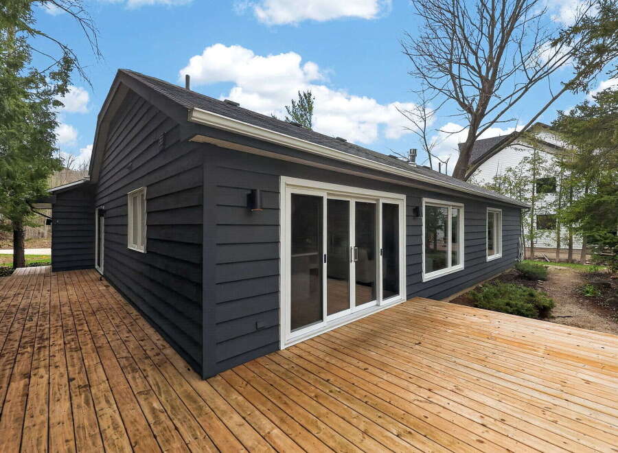 Discover this stunning property featuring a modern exterior with dark siding and a spacious wooden deck, perfect for outdoor entertaining.