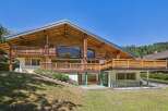 Experience luxury mountain living in this stunning wooden chalet, featuring expansive balconies with intricate carvings and breathtaking views of the surrounding landscape.