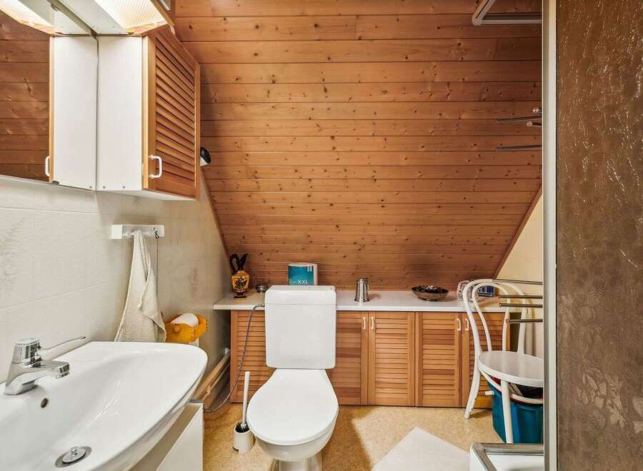 This charming bathroom features a unique sloped ceiling and warm wooden accents, creating a cozy and inviting atmosphere.