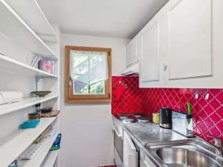 This charming kitchen features a bright red backsplash and ample storage with built-in shelving.