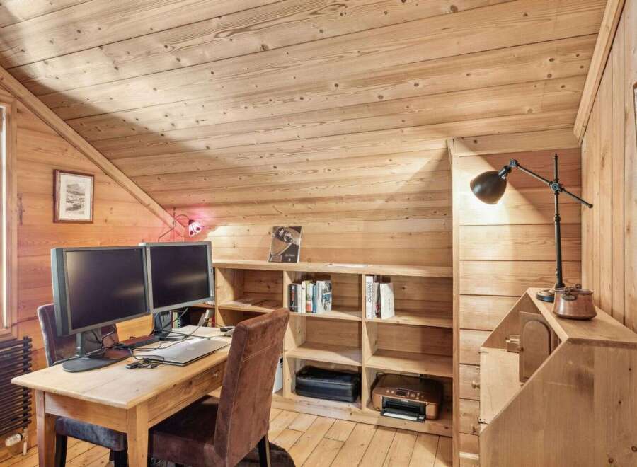 This charming home office features a warm, inviting atmosphere with its wooden walls and sloped ceiling.