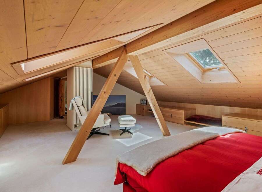 This stunning attic bedroom boasts a unique architectural design with exposed wooden beams and a sloped ceiling, creating a warm and inviting atmosphere.