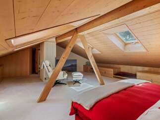 This stunning attic bedroom boasts a unique architectural design with exposed wooden beams and a sloped ceiling, creating a warm and inviting atmosphere.