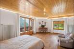 Experience breathtaking mountain views from this charming bedroom, featuring a cozy bed, a functional workspace with a desk and chairs, and a comfortable armchair.