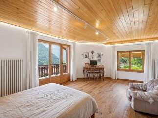 Experience breathtaking mountain views from this charming bedroom, featuring a cozy bed, a functional workspace with a desk and chairs, and a comfortable armchair.
