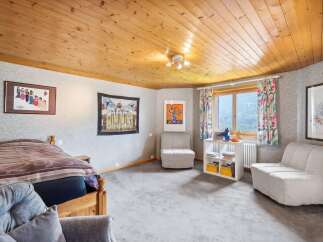 This charming bedroom features a cozy wooden bed, complemented by a soft grey carpet and a wood-paneled ceiling.