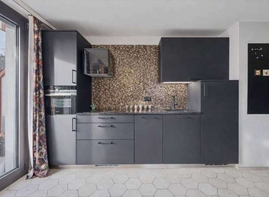 This modern kitchen boasts sleek, dark cabinetry and a stunning mosaic tile backsplash, creating a sophisticated and stylish space.
