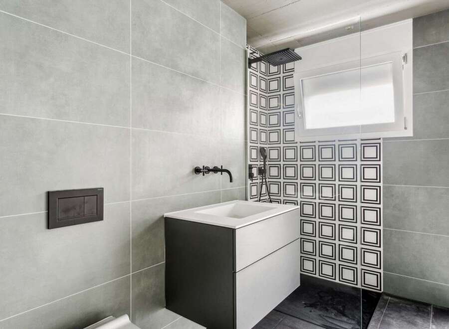 This modern bathroom features a sleek design with gray tiles and a contrasting black and white patterned accent wall.