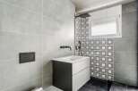 This modern bathroom features a sleek design with gray tiles and a contrasting black and white patterned accent wall.