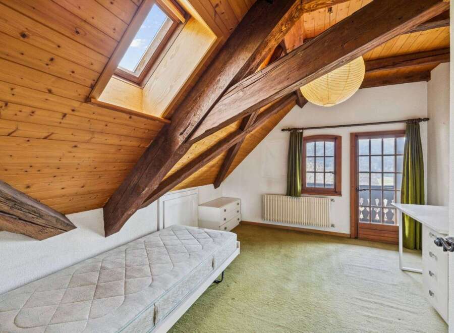 This charming attic bedroom boasts a unique architectural design with exposed wooden beams and a skylight, creating a warm and inviting atmosphere.