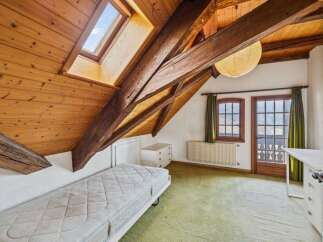 This charming attic bedroom boasts a unique architectural design with exposed wooden beams and a skylight, creating a warm and inviting atmosphere.
