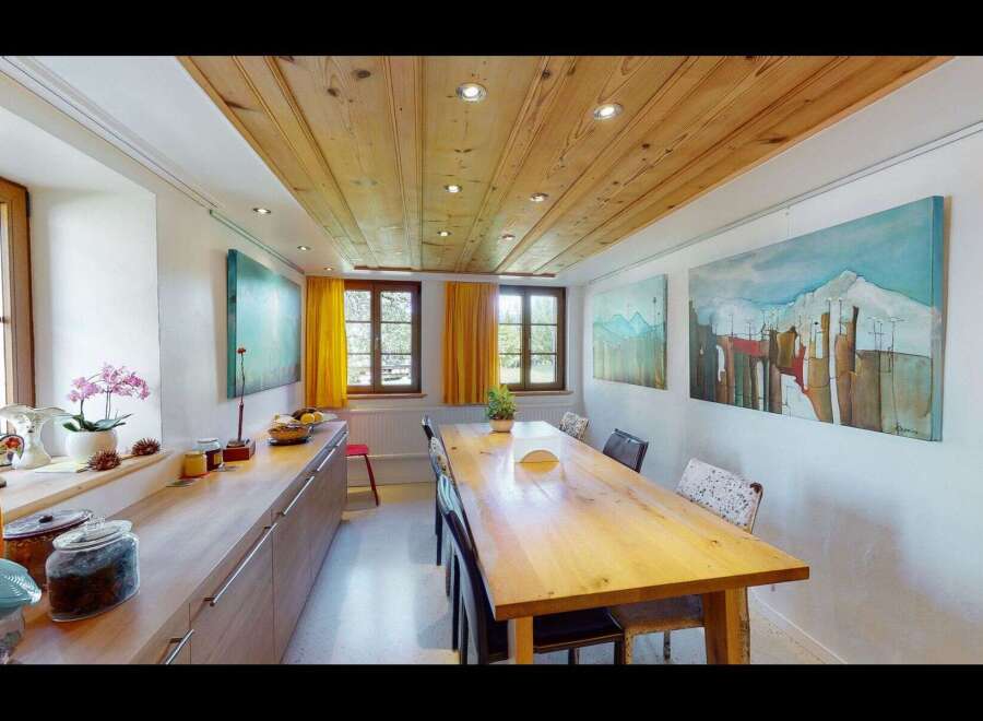 This charming dining room features a warm wooden ceiling and a long, inviting wooden table, perfect for gatherings.