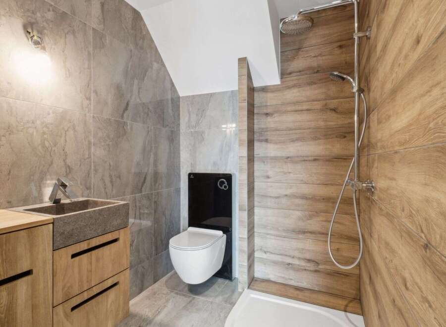 Step into a modern bathroom oasis! This stunning space features a sleek, wall-mounted toilet and a stylish wooden vanity with a stone sink.