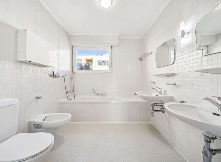 This bright and airy bathroom features a clean, minimalist design with white tile walls and flooring.