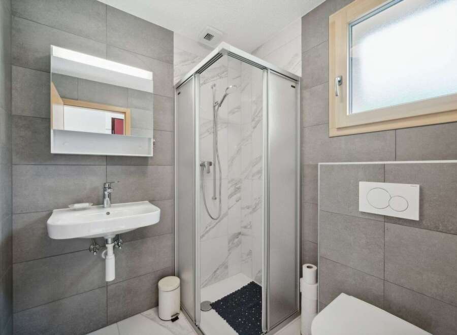 This modern bathroom features a sleek design with gray tiled walls and a glass shower enclosure.