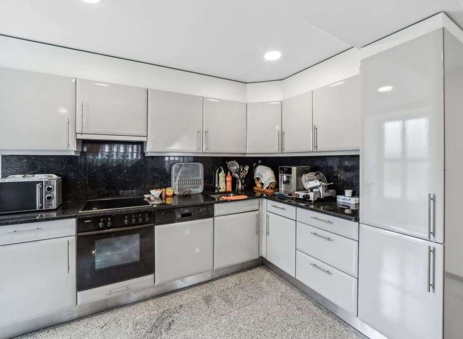 This modern kitchen boasts sleek, white cabinetry and a contrasting black countertop, creating a stylish and functional space.