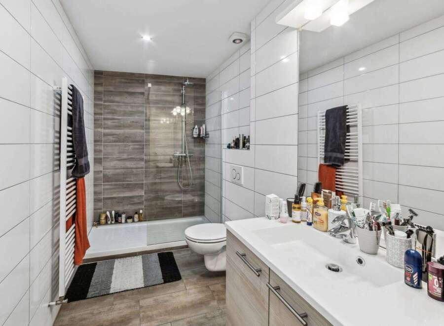 Step into a modern bathroom oasis! This stylish space features sleek white tiles, a walk-in shower with a glass door, and a contemporary vanity.